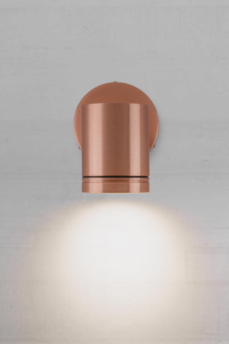 Front view with light on view of the single light, solid copper outdoor spotlight with polished finish.