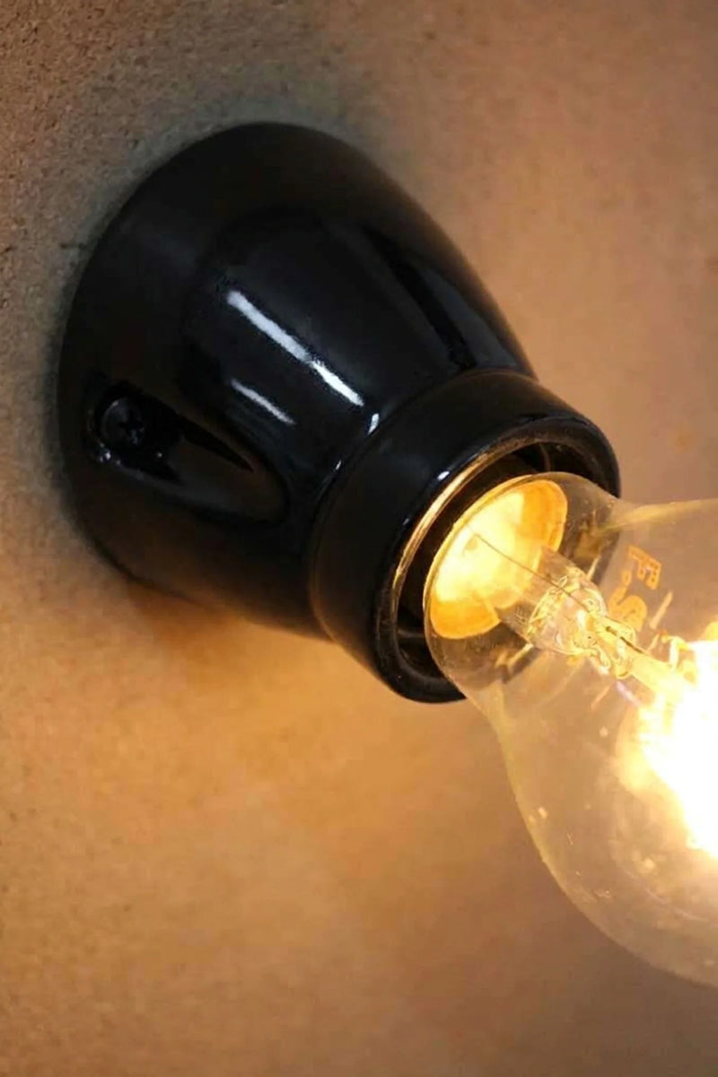 Close-up of the Delmont black glazed ceramic batten holder with an E27 bulb lit, mounted on a wall