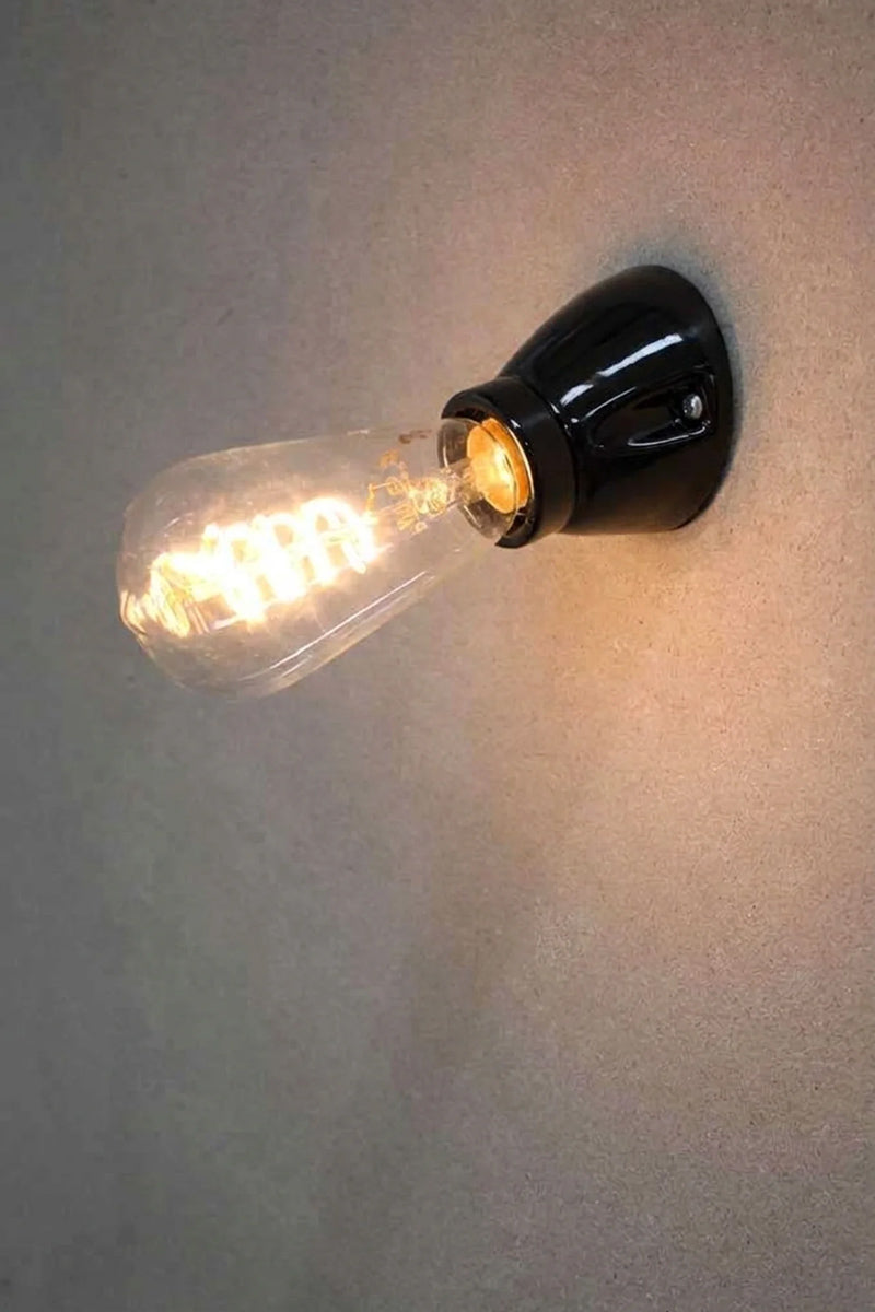 Delmont black ceramic wall mount holding a glowing vintage-style filament bulb