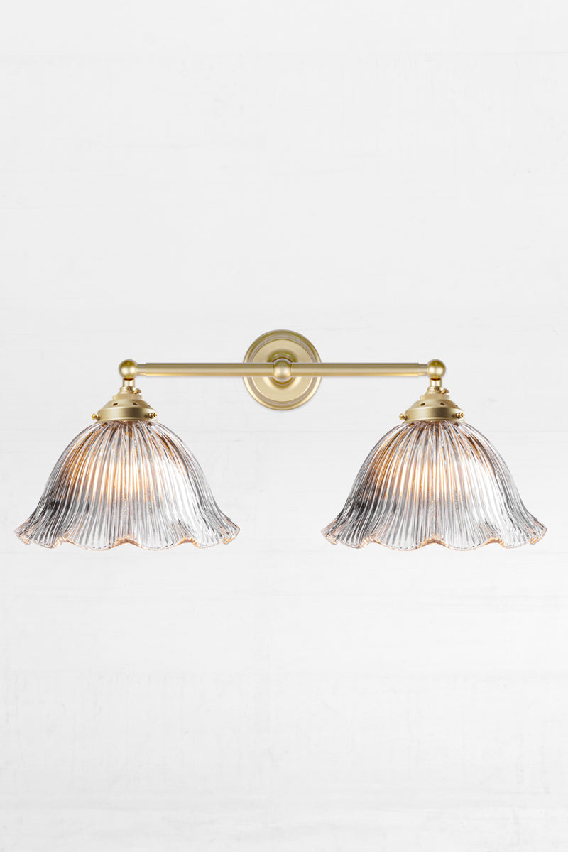 Gold/brass double swivel wall sconce with large clear glass shades with reeded detailing and a frilled edge