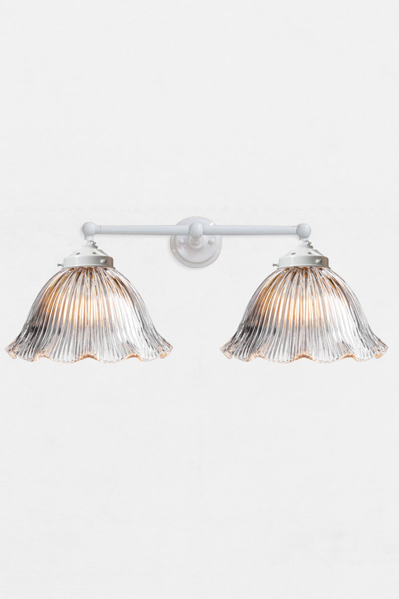 White double swivel wall sconce with large clear glass shades with reeded detailing and a frilled edge