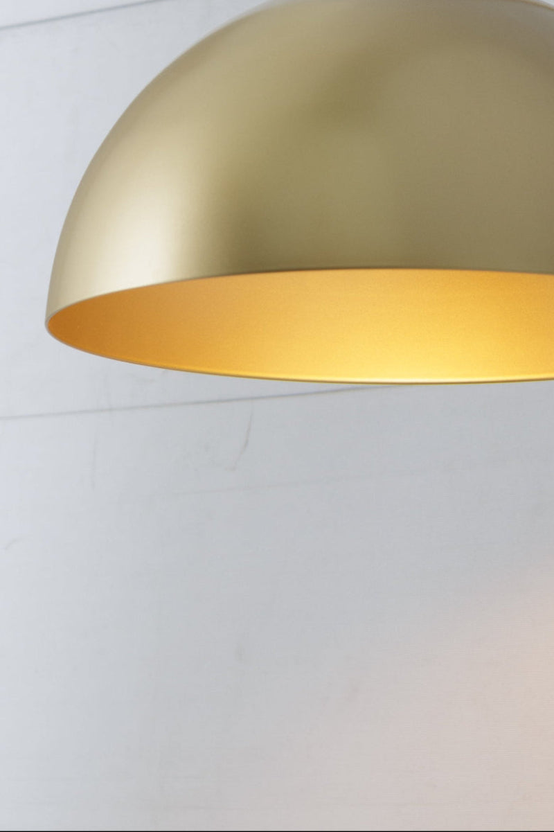 Brushed brass industrial dome pendant light suspended from a black fabric cord with warm downward illumination.