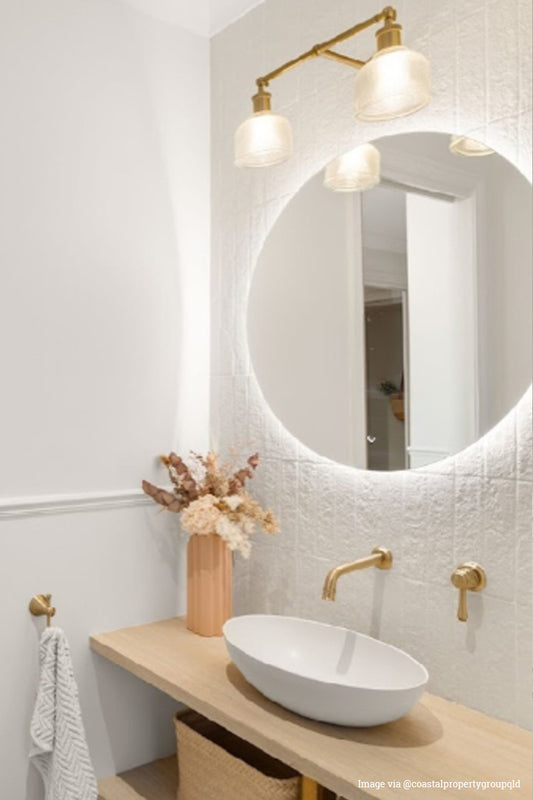 Gold/brass wall light with two holophane glass shades over a mirror in a powderroom.