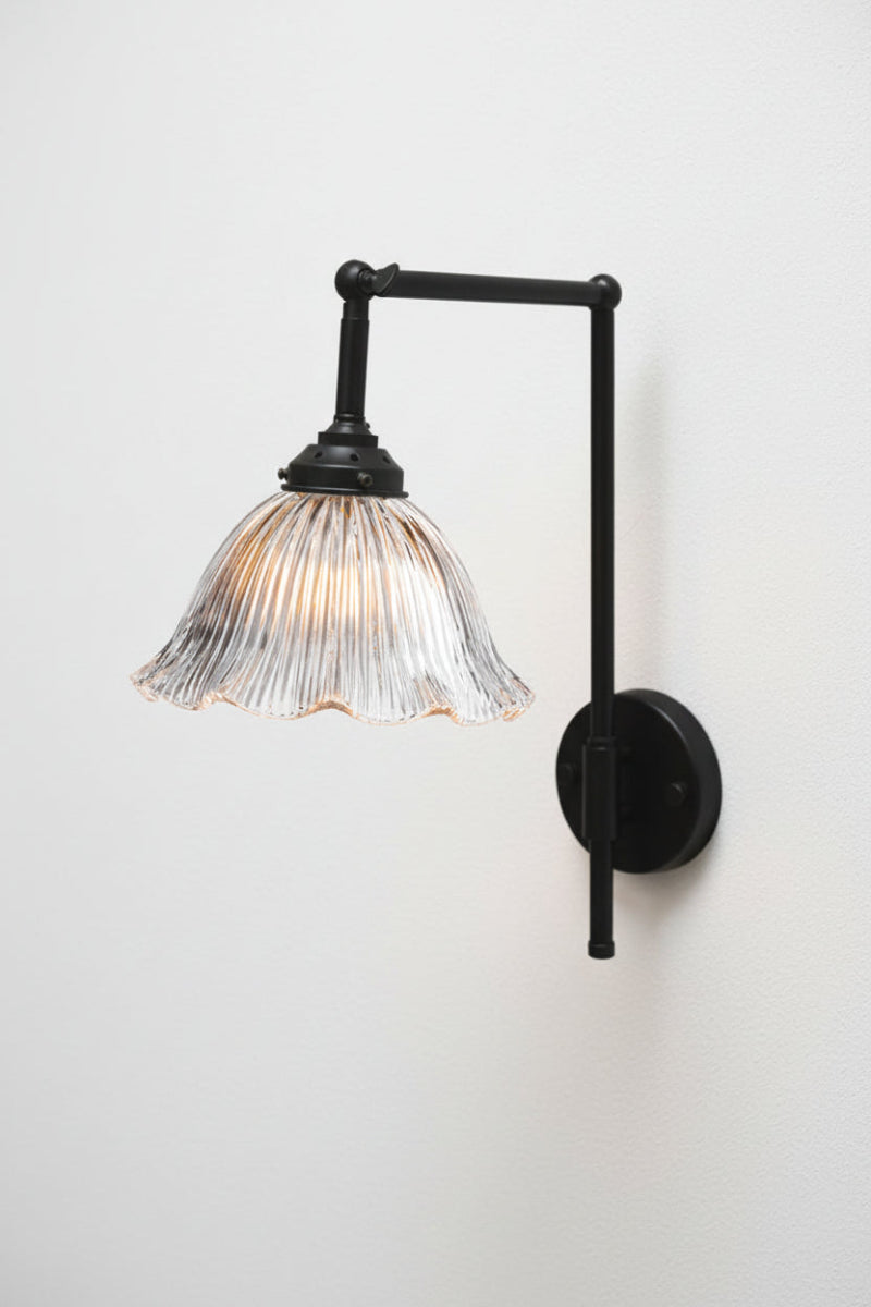 Black hook arm wall sconce with a ribbed clear glass shade featuring a frilled edge