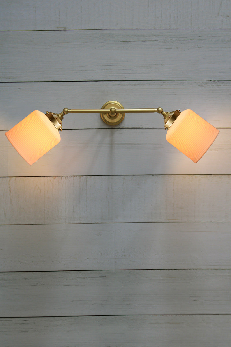 Double arm wall sconce in gold/brass with tiltable lampholders, paired with two white ceramic shades. 