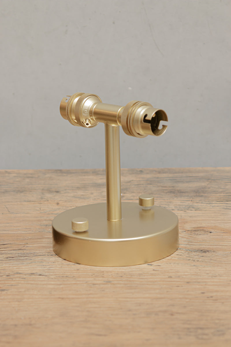 Gold/brass double wall sconce, uninstalled sitting on a timber bench. 