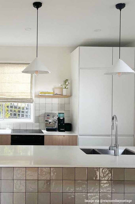 2 pendant lights with white shade over a kitchen island.