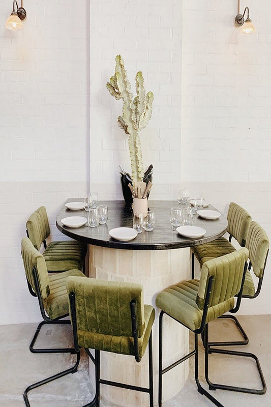 Round dining table with green chairs in a modern resturant setting with wall lights above