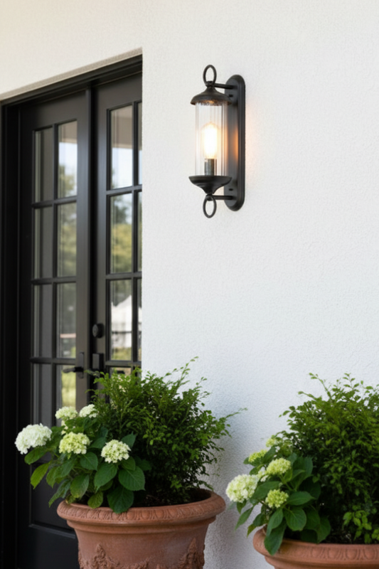 Outdoor wall light fixture on a white wall with potted plants below.