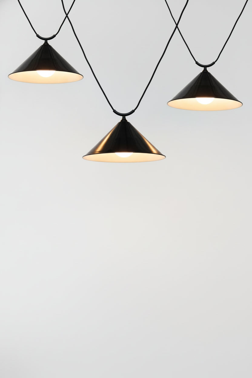 Three large black steel cone shades on trapeze pendant cords.