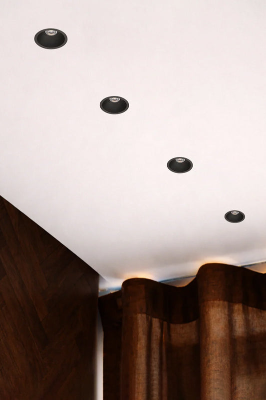 Four Black LED downlights in a white ceiling with a timber wal and curtained window. 