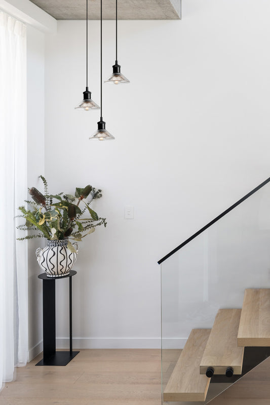 Three light multi drop pendant in black with clear reeded glass shades in a stairwell. 