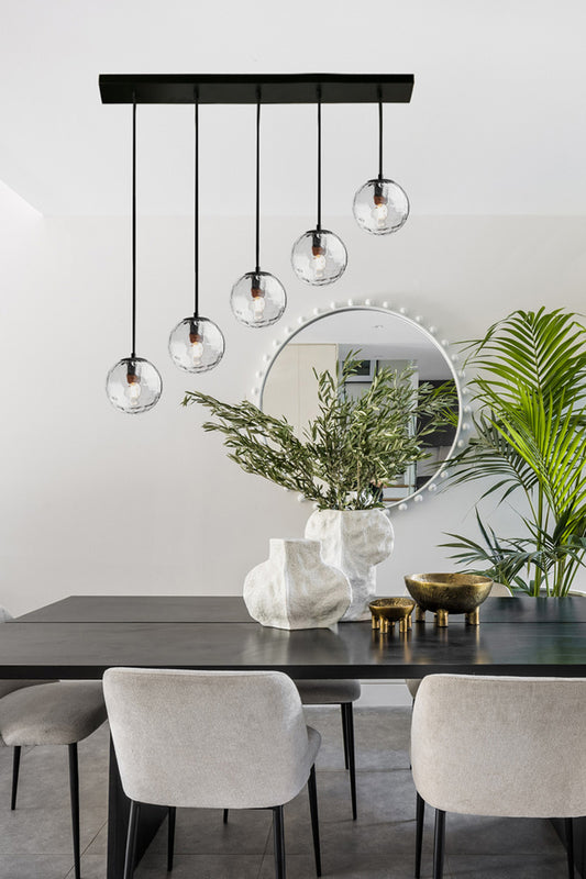 5 light clear dimpled glass ball shades on a linear pendant light over a dining space. 