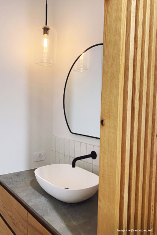 Single cylindar shaped clear glass shade on a black bendant cord in a modern powder room in white, black, concreate and timber finishes. 
