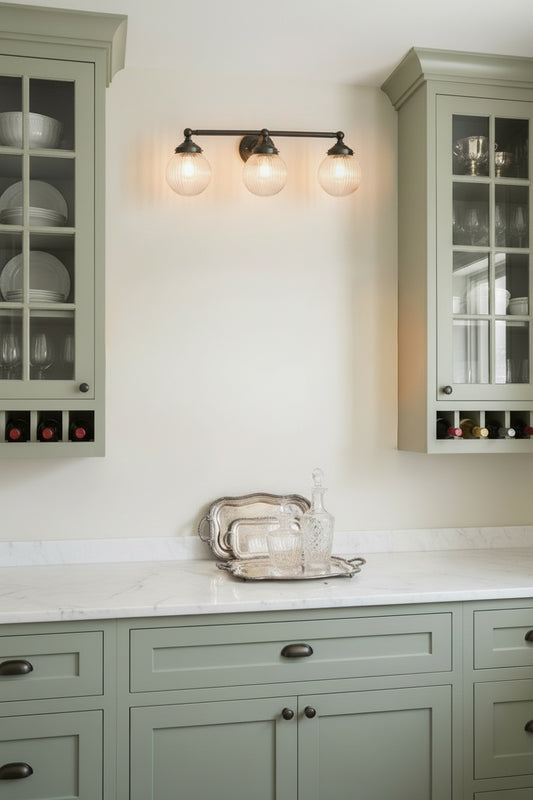 Two, 3 lampholder wall sconce in black with clear reeded glass ball shades over a white kitchen space, butlers pantry 
