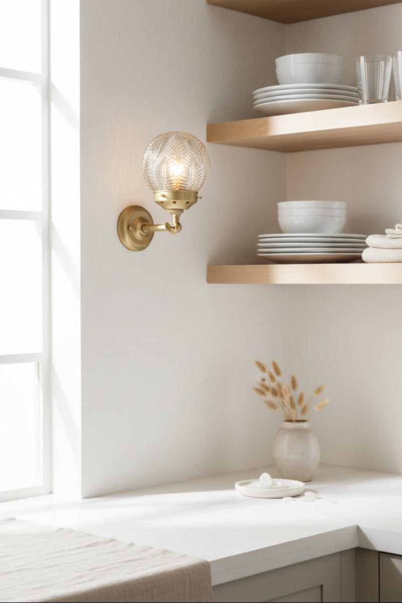 Gold/brass straight arm wall sconce with detailed clear glass shade in an open and bright butlers pantry