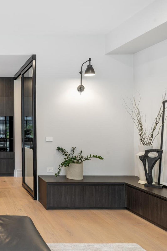 Black wing arm wall scone with black metal shade in a modern lounge corner. 
