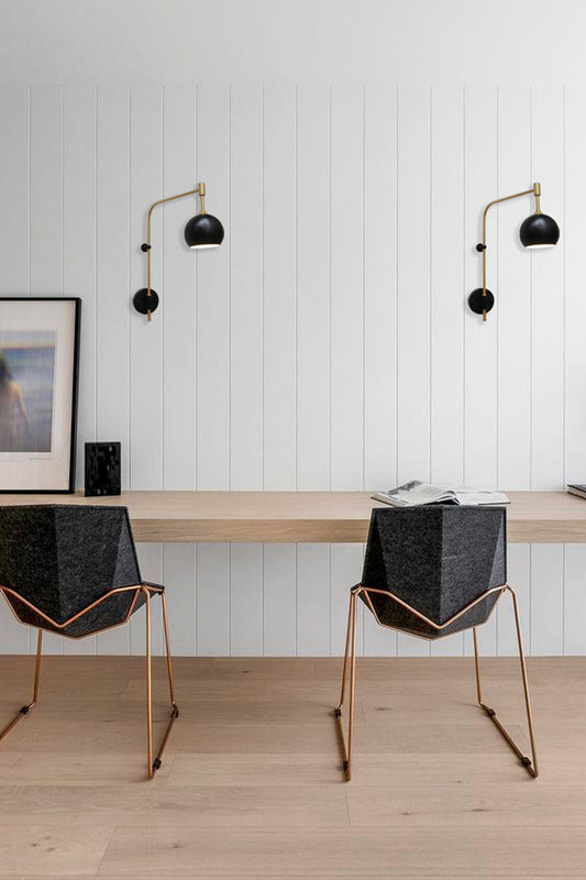 Two gold/Brass wing arms with black accents and bulb shades over a desk space. 