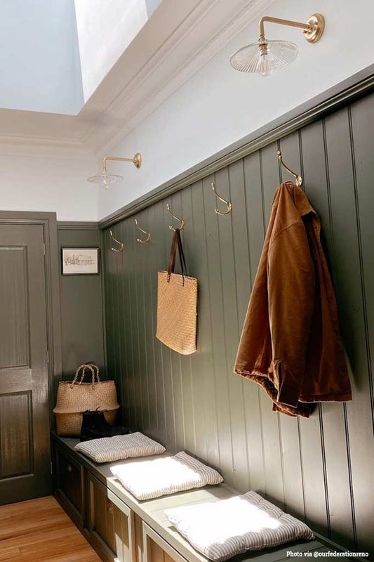 Two gold and glass wall lights hanging in a sage green mud room.