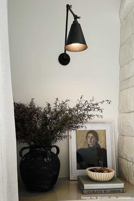 A brass cone shade swing arm wall light hanging above a vase.