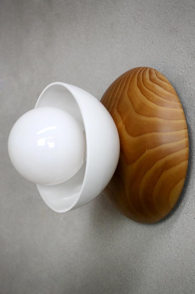 A wall Mount Light with a natural wood timber base and a genuine Bakelite bowl shade in white, illuminated by a bulb.