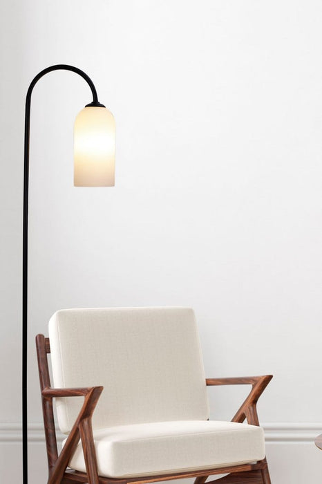 Floor lamp with opal glass shade placed next to a chair against a white background. 