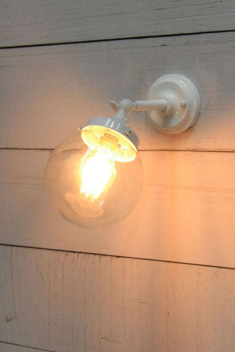 Glass ball wall light with short white arm and small clear shade in tilted position