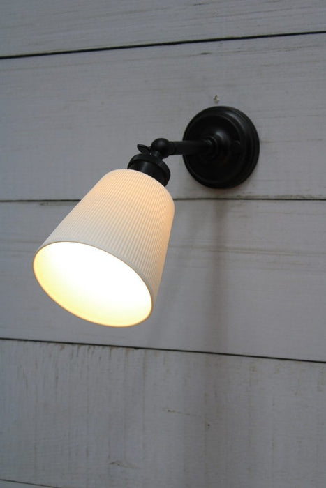 Swivel arm wall light with black sconce and large ceramic shade tilted on an angle