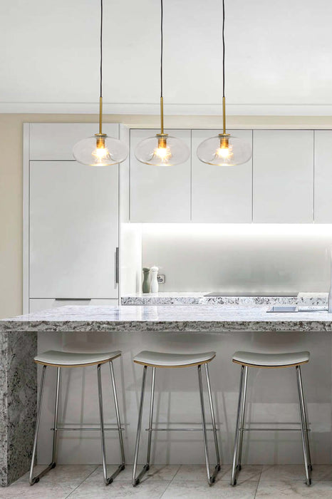 three glass pendant lights in the gold/brass finish hung from ceiling within a kitchen interior. 