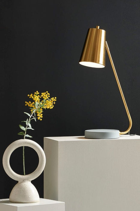 Satin brass table lamp on a cubed box with a wattle flower and black background