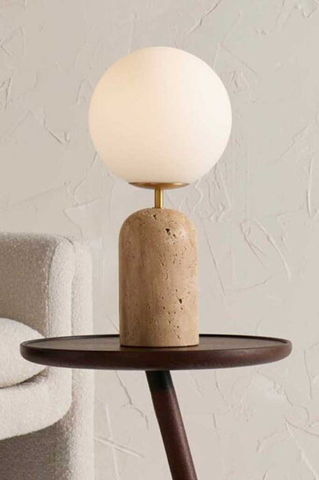 Opal glass table lamp with travertine base over a coffee table.