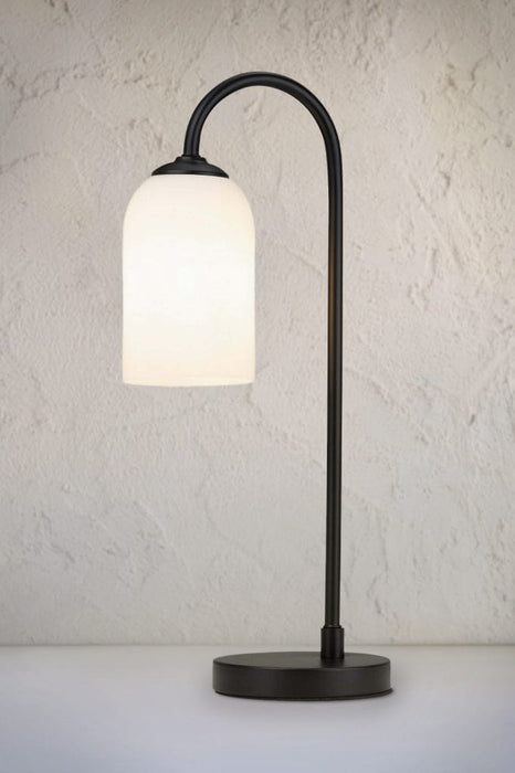 Table lamp with cylindrical frosted opal glass shade and black metalware build on a smooth surface. 