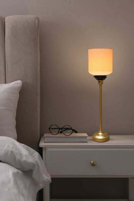 Ribbed ceramic shade with a gold candlestick lamp base set in a bedroom
