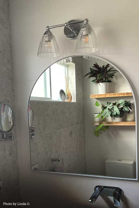 Double chrome and glass wall light over a mirror in a bathroom.