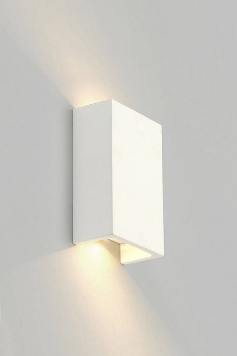 Up and down rectangular plaster wall light in white lit up and affixed on wall.
