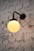 Brass wall light in a black finish with small ridged opal glass ball shade