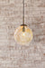 Small amber glass pendant light against white washed brick wall. 