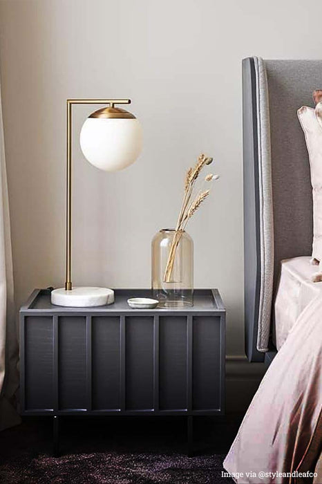 Brass light with opal shade and marble base over bedside table.