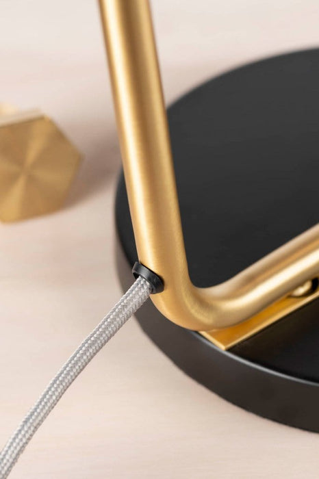 Detail of round black table lamp base and gold fixture with a grey braided fabric power cord