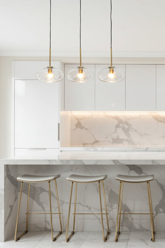 three glass pendant lights in the gold/brass finish hung from ceiling within a kitchen interior. 