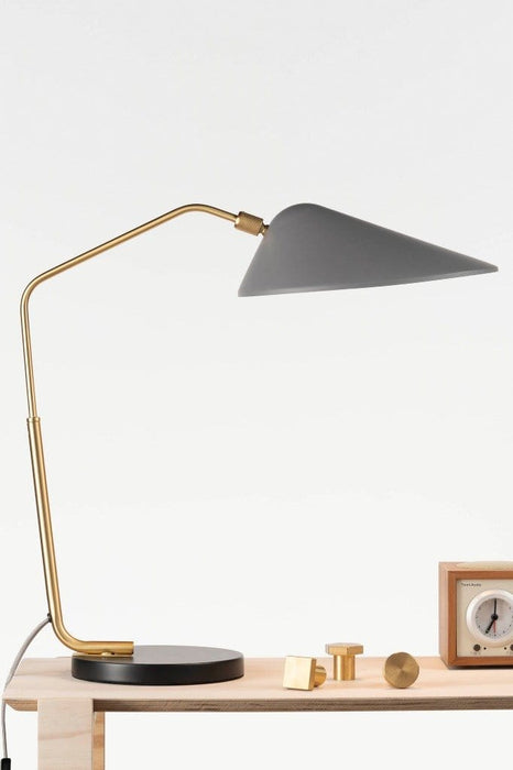 Table lamp with round black base, gold brass arm and satin grey shade on timber table