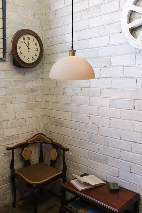 opal glass pendant with gold pendant cord against a white brick wall